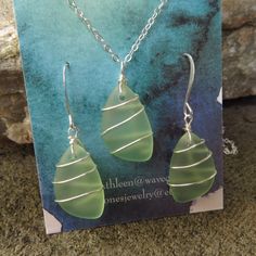 a pair of green earrings sitting on top of a card next to a stone wall