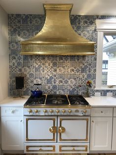 a stove top oven sitting inside of a kitchen under a gold hood over it's burner