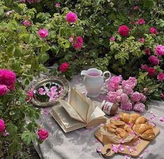 an open book on a table surrounded by pink flowers and other items in front of it