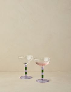 two wine glasses sitting side by side on top of a white table with pink and green rims