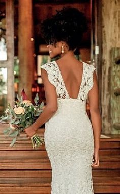 a woman standing in front of a wooden bench wearing a white dress with open back