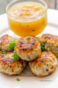 crab cakes on a white plate next to a bowl of mustard and a glass of orange juice