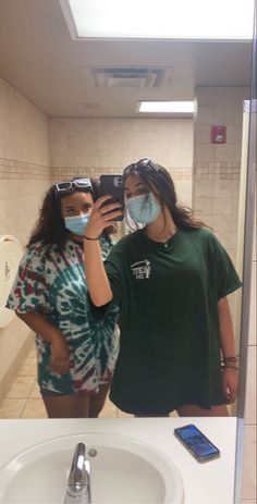 two women wearing face masks are taking a selfie in the bathroom mirror with their cell phones