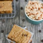 peanut butter and chocolate chip cookie bars are stacked on top of each other in front of a bowl of peanuts