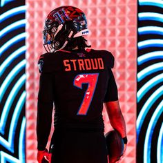 a football player wearing a black uniform and holding a ball in front of a neon background