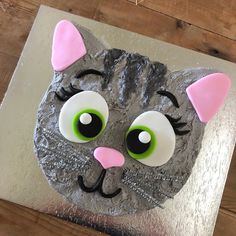 a cake decorated to look like a cat's face with green eyes and pink ears