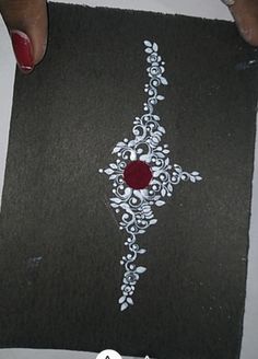 someone is painting on a piece of black paper with white and red designs in it