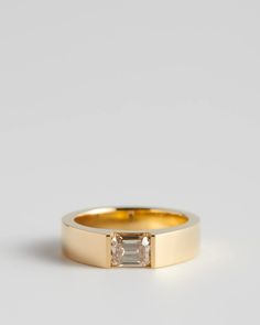 a yellow gold ring with a baguette cut diamond in the center, on a white background