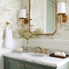 a bathroom with green cabinets and gold fixtures on the mirror above the sink is a vase with flowers in it