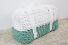 a white and green crocheted bag sitting on top of a wooden table next to a wall