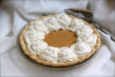 a pie with whipped cream on top is sitting on a white cloth next to a spoon