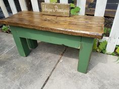 a green bench sitting on top of a cement ground next to a white picket fence