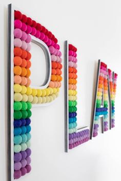 the word play spelled with multicolored pom - poms on a white wall