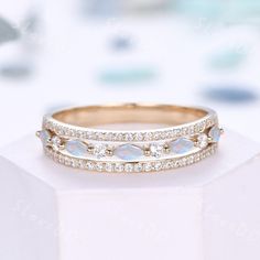 two wedding bands with opal and diamonds on top of a white pedestal in front of some other items