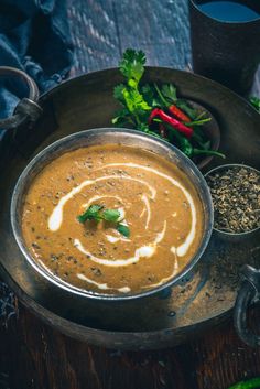 a metal bowl filled with soup next to other foods on a wooden table and spoons