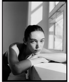 a black and white photo of a woman leaning on a window sill