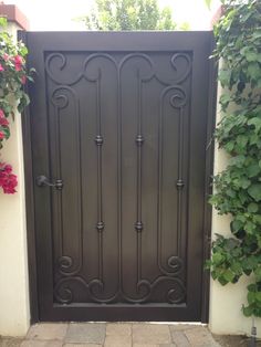 an iron gate in front of a house with flowers growing on the wall and behind it is a brick walkway