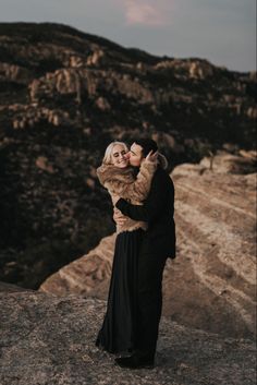 an engaged couple embracing on top of a mountain