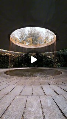 a circular fountain in the middle of a courtyard with trees and bushes on either side