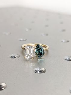 an emerald and diamond ring sitting on top of a table