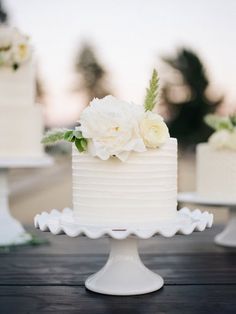 three tiered wedding cake with white flowers on each layer and greenery at the top