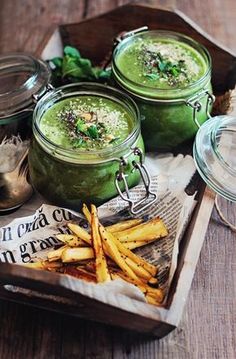 three mason jars filled with green smoothie and french fries on a wooden tray next to some parmesan cheese