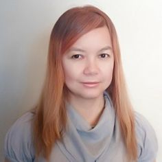 a woman with long red hair wearing a gray shirt and posing for a photo in front of a white wall