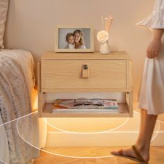 a woman standing next to a night stand with a photo on it and an electronic clock