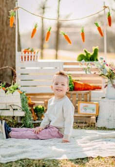 a little boy sitting on the ground in front of some carrots and bunting