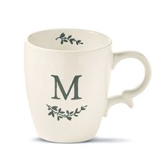 a white coffee cup with the letter m on it's side and leaves in the middle