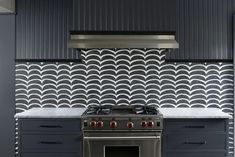 a stove top oven sitting inside of a kitchen next to a wall covered in black and white tiles