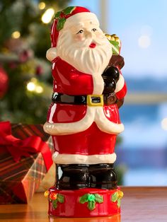 a santa clause figurine sitting on top of a table next to a christmas tree