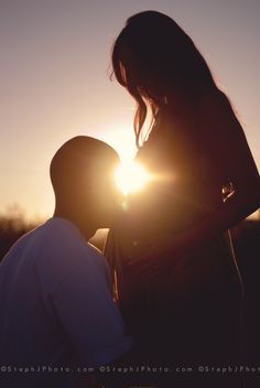 two people standing next to each other in front of the sun with their faces close together