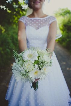 a woman in a dress holding a bouquet of white flowers and greenery on her wedding day