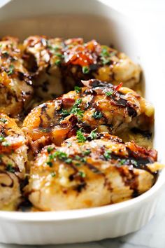 a white bowl filled with chicken covered in sauce and garnished with parsley