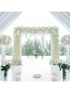 an outdoor wedding setup with white flowers and greenery on the aisle, surrounded by tall pillars