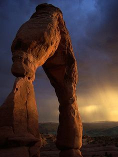 an arch shaped rock formation in the desert under a cloudy sky with sunbeams