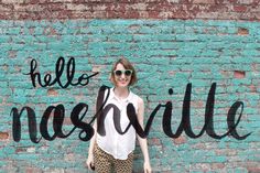 a woman standing in front of a brick wall with the words hello masvillee painted on it