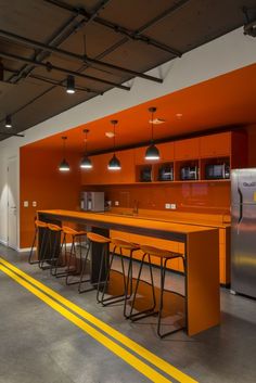 an orange kitchen with bar stools in the center and refrigerator on the other side