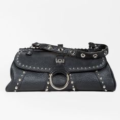 Crafted From Grained Black Leather, This Chic Dolce & Gabbana Baguette-Style Shoulder Bag Features A Silver-Tone Decorative Front Ring Detail Hanging From A Buckled Leather Strap, Silver-Tone Studs Throughout, And A Black Alligator Handle With Reinforced Eyelets. The Flap Is Secured By A Magnetic Snap Closure And Opens To A Leopard-Printed Nylon Interior With A Zip Pocket. Condition: Good; Faint Slouching, Visible Wear On Side Exterior Leather, Minor Markings On Hardware, Faint Patina And Wear On Handle. Approximate Measurements: Height: 7” (13 Cm) Width: 15” (38 Cm) Depth: 5” (13 Cm) Handle Drop: 8” (20 Cm) Composition: Calfskin Leather, Alligator Trims, Metal Hardware Black Alligator, Black Shoulder Bag, Metal Hardware, Snap Closure, Calf Skin, 20 Cm, Leather Straps, Zip Pockets, Dolce And Gabbana