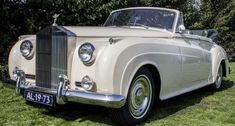 an old white car parked on top of a lush green field