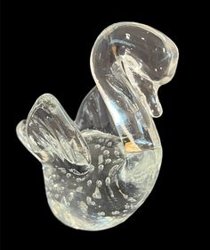 a clear glass duck sitting on top of a black surface with bubbles in it's beak