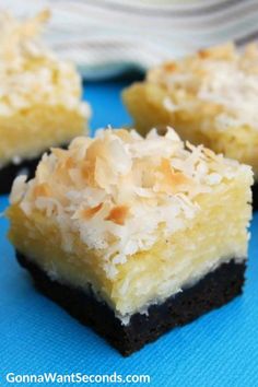 three pieces of cake with coconut toppings on a blue tablecloth and one piece is cut in half