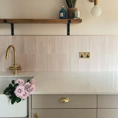 a white kitchen with pink tiles and gold handles on the wall above the sink is a potted plant