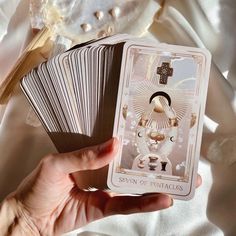 a person holding up some cards on top of a white cloth covered tablecloth with an image of the seven of pentacles in it's center