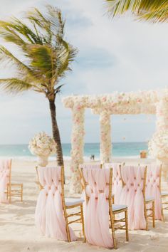 an outdoor wedding setup with pink chiffon chairs and white flowers on the beach