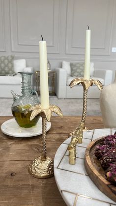 two candles sitting on top of a wooden table next to plates with food and vases