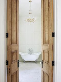 an open door leading to a bathroom with a tub and chandelier