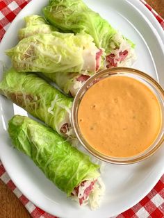 lettuce wrapped in leafy greens with dipping sauce on the side, sitting on a white plate