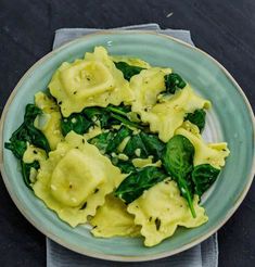 a green plate topped with ravioli and spinach on top of a white napkin